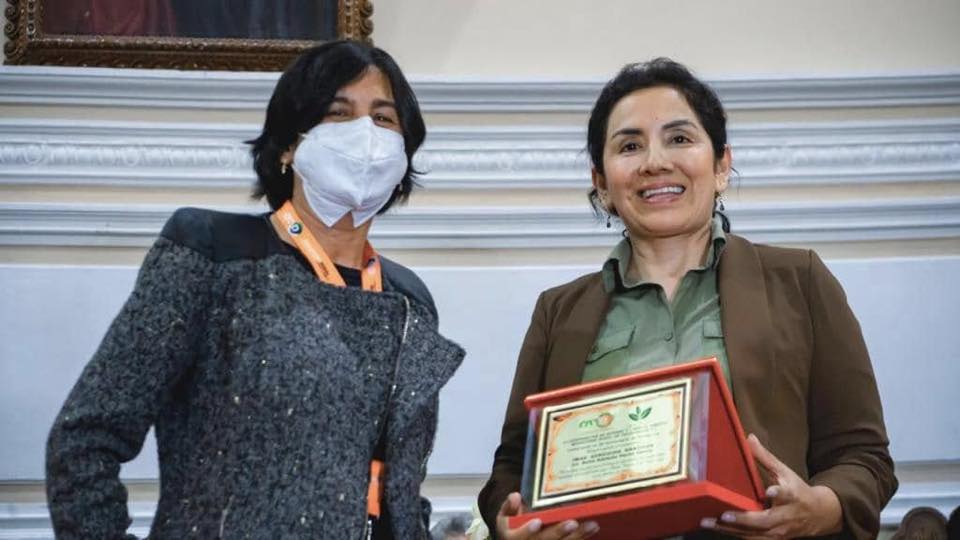 Dos mujeres en ceremonia de reconocimiento con certificado